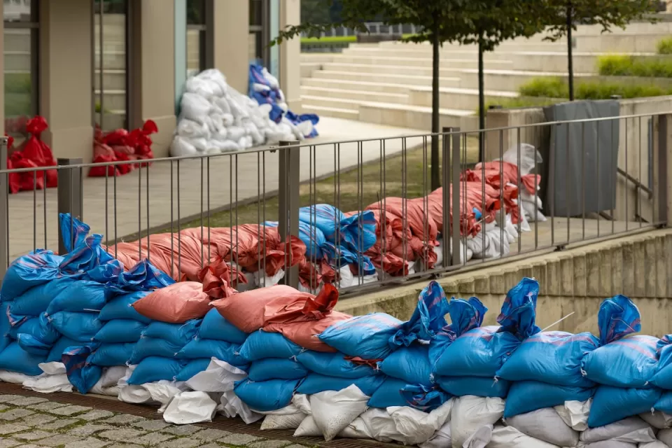 Red, white, and blue sandbags stacked along bridge railing and building doors and windows.